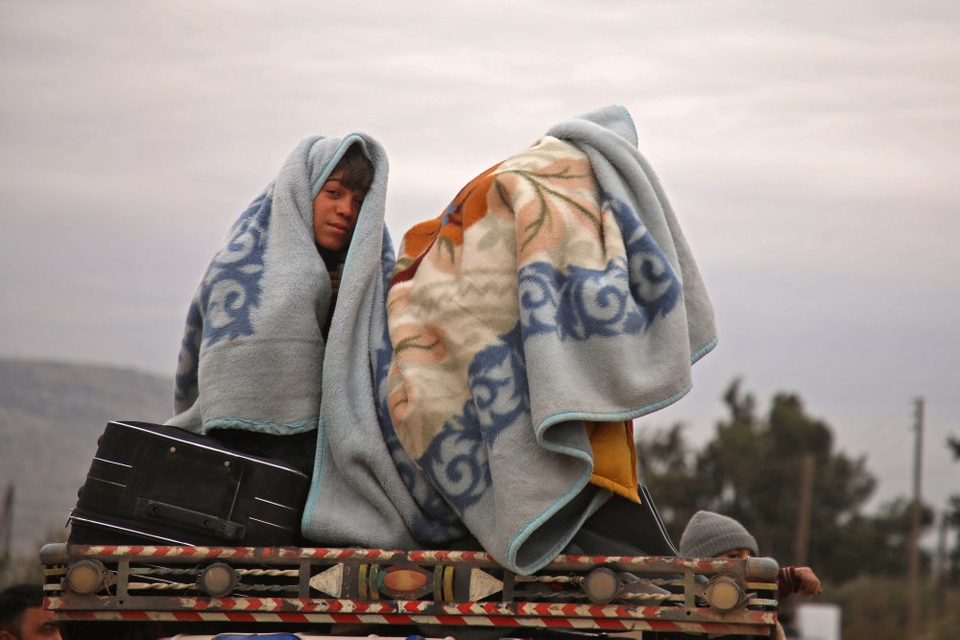 Syriske børn har pakket sig ind i tæpper, mens de den 11. februar 2020 sidder bag på en lastbil nær byen al-Ghazawiya og flygter fra angreb på landbrugsområder vest for Aleppo.